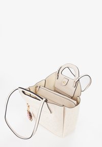 Beige tote bag med præget blomsterdesign, sort kant og dobbelt hanke; har en indvendig lomme og guldfarvet hardware.
