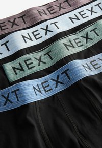 Vīriešu apakšveļas multipakotne ar krāsainām elastīgām jostām gaiši pelēkā, zaļā un zilā krāsā, kurās ir burtiski izsaukuma 'NEXT' melniem lielajiem burtiem.
