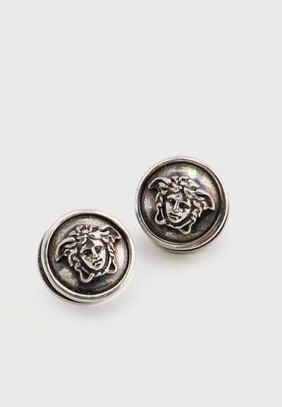 Ζευγάρι στρογγυλών ασημένιων μανικετοκουμπιών με ανάγλυφη κεφαλή Μέδουσας σε σκουρόχρωμο φόντο.
