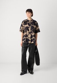 Kortermet skjorte i beige med store svarte blomsterdesign, sammen med svarte skinnbukser og en plisserte svarte totebag.
