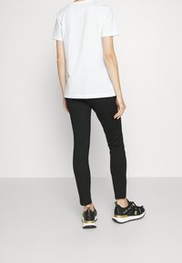 Czarne legginsy w połączeniu z prostą białą koszulką o minimalistycznym wzorze. Model nosi czarne i złote sneakersy z dodatkowym wykończeniem.