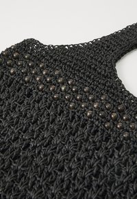 Borsa a tracolla nera intrecciata con un design testurizzato, caratterizzata da perline scure e rotonde cucite nella sezione superiore per un tocco di stile.