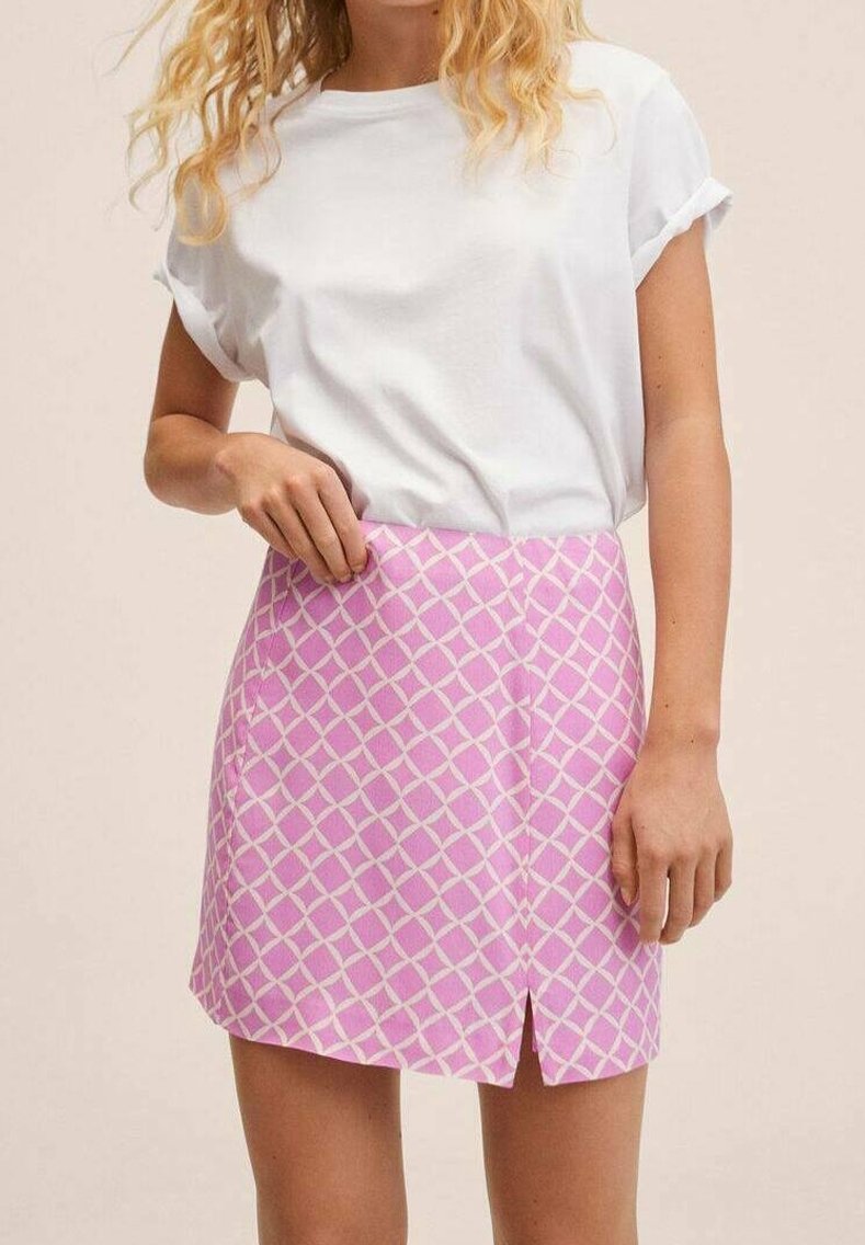 Femme portant un t-shirt blanc à manches retroussées et une mini-jupe rose avec un motif losanges blancs et une fente à l'avant.