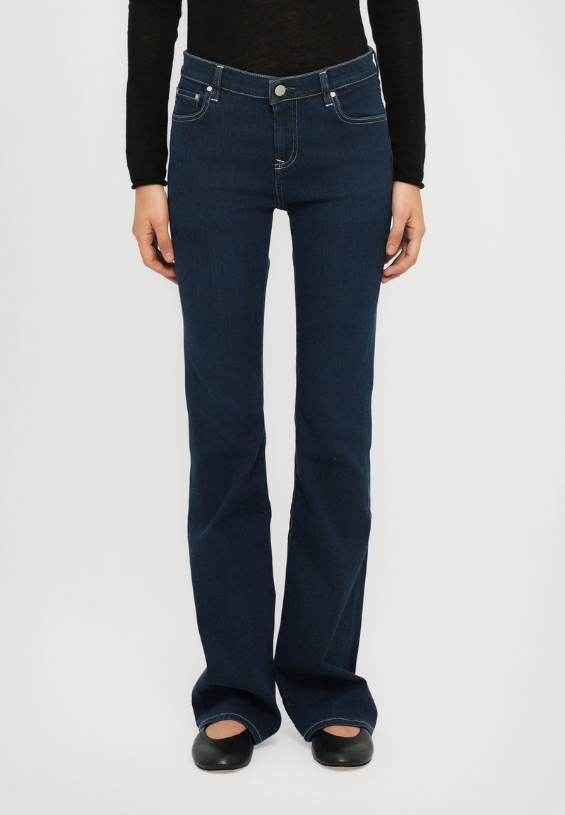 Jeans acampanados de color azul oscuro con una cintura alta, bolsillos frontales y cierre de botón metálico. Elaborados en denim con una textura suave.