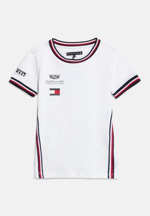 Tricou alb cu mâneci scurte Tommy Hilfiger, cu garnitură bleumarin și roșie, cu logo-urile Cadillac Formula 1 Team și Pirelli pe față și mânecă.