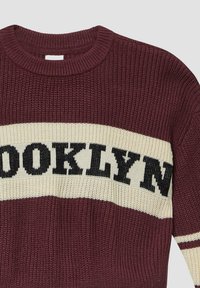 Gebreide trui in bordeauxrood met crèmekleurige en zwarte strepen. Heeft "BROOKLYN" in vette letters over de borst, met ribgebreide ronde hals en manchetten.