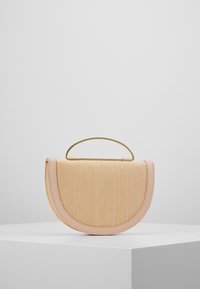 Beżowa torebka w kształcie półksiężyca, z jasnoróżowym wykończeniem i zakrzywionym złotym metalowym uchwytem, na białym pedeście.