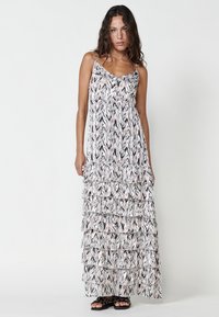 Robe maxi à fines bretelles, présentant un motif zigzag blanc, noir et rose, avec des volants superposés et une texture de tissu fluide et douce.
