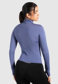 Langärmliges, tailliertes Oberteil aus helllila Stoff mit hohem Kragen, das eine glatte Textur und nahtloses Design bietet, kombiniert mit schwarzen Leggings.