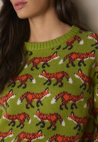 Green knitted sweater featuring an all-over design of red foxes, with black accents and white tails. Ribbed neckline adds texture.