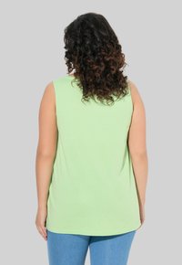 Top senza maniche verde chiaro, materiale in cotone morbido, vestibilità comoda, orlo arrotondato, texture semplice, abbinato a jeans blu.