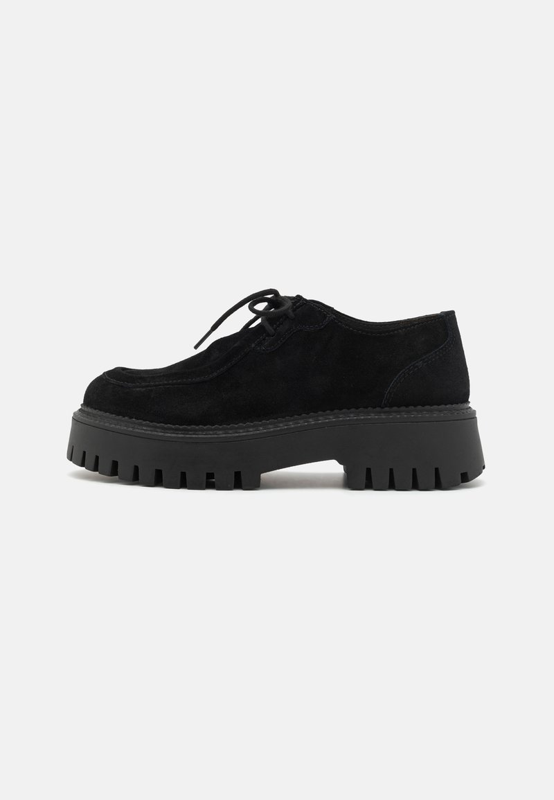 Scarpe nere in suede con lacci e suola a piattaforma caratterizzata da scanalature profonde, punta arrotondata e cuciture resistenti lungo il bordo.