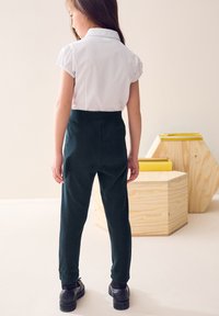 Fehér galléros ing rövid fodros ujjakkal, sötétzöld, testhezálló nadrággal és fekete cipővel párosítva. Egyszerű, tiszta dizájn, látható minták nélkül.