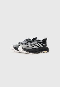 Baskets noires et blanches avec un upper en mesh, semelle en caoutchouc, design texturé et accents réfléchissants. Comprend des lacets et une sangle de traction.