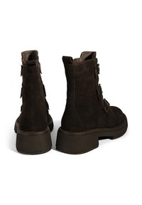 Braune Wildleder-Stiefeletten mit dicker Sohle, ausgestattet mit einem seitlichen Reißverschluss, drei dekorativen Schnallen an der Außenseite und einer abgerundeten Zehenpartie.