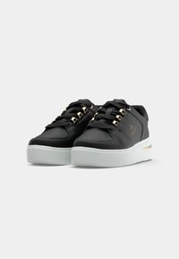 Czarne sneakersy wykonane z syntetycznej skóry o teksturowanym wykończeniu, z ozdobnymi oczkami w złotym kolorze, czarnymi sznurowadłami i białą platformą.