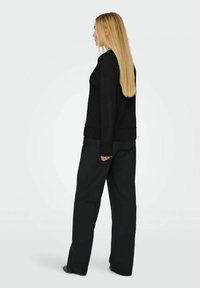 Maglione nero a maglia con una vestibilità rilassata e polsini a coste, abbinato a pantaloni neri larghi. Capelli lunghi e lisci visibili di lato.