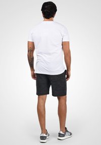 Camiseta blanca de manga corta, pantalones cortos grises con un patrón texturizado y zapatillas deportivas grises. La vista desde atrás muestra un ajuste relajado.