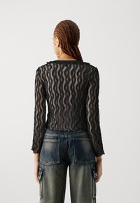 Svart spets topp med långa ärmar som har ett vågigt mönster och en figurnära silhuett, visas med högmidjade blå denim cargo byxor.