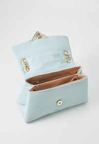 Sac pochette rectangulaire bleu clair en matériau lisse, avec un fermoir triangulaire en or, des compartiments intérieurs et un éclat subtil.