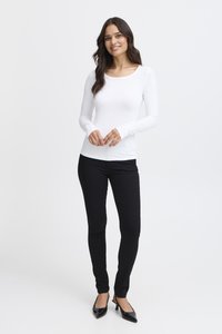 Valkoinen pitkähihaisen puseron yläosa, jossa on pyöreä pääntie, yhdistetty mustiin istuviin housuihin ja mustiin korkeakorkoisiin kenkiin. Sileä kangas ilman kuvioita.