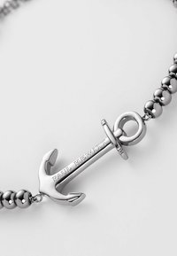 Pendente ad ancora in argento con incisione in rilievo "Paul Hewitt", attaccato a una catena metallica con perline. Texture liscia, finitura lucida.