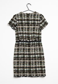 Tweedové šaty s krátkými rukávy, zdobené kostičkovaným vzorem v černé, bílé, zelené a zlaté barvě. Součástí je černý pásek v pase a zapínání vzadu.
