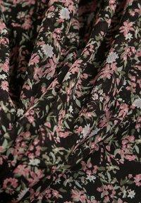 Tela negra con un patrón floral en rosa, azul y verde. La textura es suave con pliegues sutiles y detalles de caída.