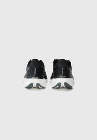 Baskets de sport noires avec un dessus en maille texturée, une semelle intermédiaire blanche et un motif de semelle en caoutchouc ; elles présentent des accents réfléchissants sur le talon.