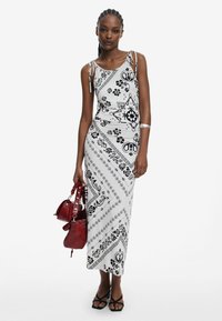 Schwarz-weiß bedrucktes Maxikleid mit Spagettiträgern und Blumenmuster, kombiniert mit einer roten Handtasche und schwarzen High Heels.