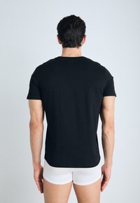 Zwarte katoenen t-shirt met ronde hals, korte mouwen en een standaard pasvorm, gezien vanuit de achterkant. G gedragen met witte boxershorts.