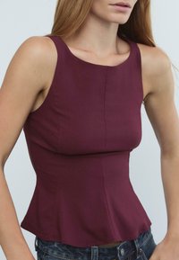 Top peplum bordeaux realizzato in tessuto morbido con scollo rotondo e corpino aderente, che termina con un orlo a balze.