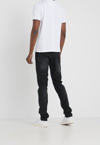 Valkoinen poolopaita, jossa mustat reunukset, yhdistetty kapeisiin mustiin farkkuihin. Jalkineet ovat valkoiset ja yksinkertaiset. Minimalistinen yleisilme.