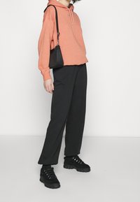 Orange huvtröja med dragsko, svarta skräddarsydda byxor och chunkiga svarta sneakers. Komplett med en liten svart axelväska.