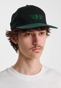 Black baseball cap with a green visor and embroidered logo in green. The cap features a structured crown and adjustable back strap.