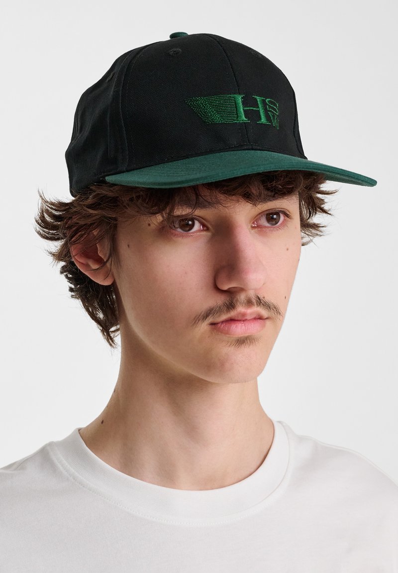 Zwarte honkbalpet met een groene klep en geborduurd logo in het groen. De pet heeft een gestructureerde kroon en een verstelbare achterkant.