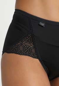 Black high-waisted underwear featuring smooth fabric and a lace panel on the sides, detailed with delicate scalloped edges and a logo tag.