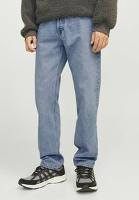 Vaqueros de mezclilla azul claro con un diseño de pierna recta, que presentan costuras visibles y bolsillos. Combinados con zapatillas deportivas negras y grises.