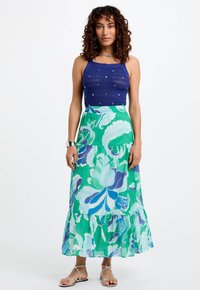 Top in cotone azzurro all'uncinetto con perline decorative, abbinato a una gonna maxi fluida verde, blu e bianca con motivo floreale, caratterizzata da un orlo arruffato.