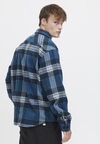 Blauwe geruite flanellen overhemd met zwarte en witte accenten, met knoopmanchetten en een puntige kraag. Relaxte pasvorm en gestructureerde stof.