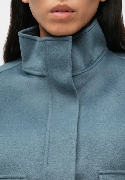 Jasnoniebieska kurtka z mieszanki wełny z wysokim kołnierzem, charakteryzująca się czystymi liniami i minimalistycznymi detalami; miękka w dotyku i o eleganckim kroju.