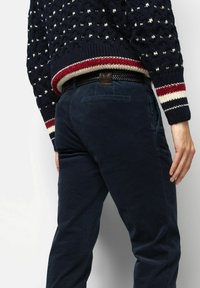 Navy corduroy pants with a slim fit, featuring back pockets and a brown leather label. The sweater has a textured knit and striped cuffs.