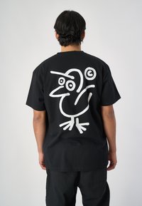 Schwarzes Baumwoll-T-Shirt mit großem weißen Cartoon-Vogel-Graphic auf dem Rücken. Kurze Ärmel, runder Ausschnitt, entspannte Passform.