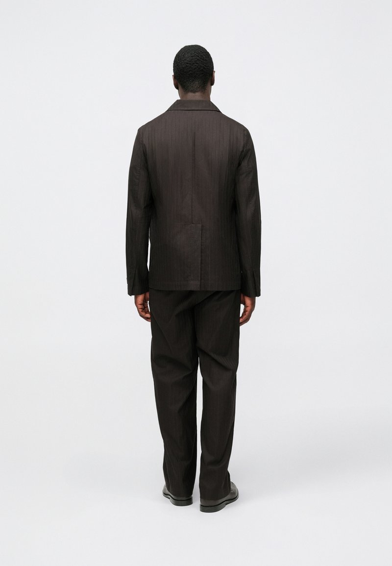 Bruin gestreept pak bestaande uit een blazer en bijpassende broek. De stof heeft een gladde textuur. Voorzien van een ingesneden revers en standaard achterkant.