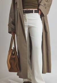 Bēša tranšejas mēteli pāri olīvzaļai tvertnei, apvienots ar baltām paplašinātām biksēm. Brūna zamša rokassoma ar rāvējslēdzēju un austs melns jostas.