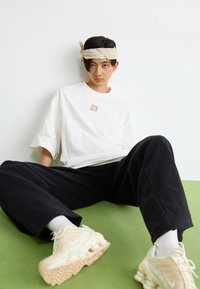 Fehér, oversize póló, texturált függőleges csíkokkal és arany "23" grafikával, fekete lazán illeszkedő nadrággal és bézs Nike tornacipővel Párosítva.