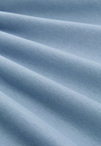 Mīkstus gaismas zila auduma ar vienmērīgu, gludu drapējumu, kas izceļ tā smalkās teksturētās austas un matētas virsmas.