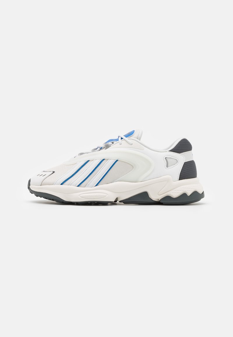 White athletic shoe with mesh and synthetic overlays, featuring three blue stripes, grey accents, and a wave-patterned sole.