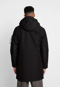 Czarna wodoodporna parka z kapturem, elastycznymi mankietami i kontrastowymi akcentami materiałowymi na ramionach. Posiada zabezpieczoną kieszeń na suwak na rękawie.