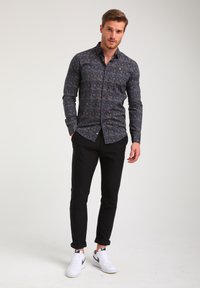 Camisa de manga larga, de color navy, con un patrón floral, combinada con pantalones ajustados negros y zapatillas blancas. Presenta un cuello abotonado y un diseño entallado.